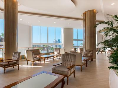 Lichte lounge met grote ramen, comfortabele stoelen en planten in een hotel.