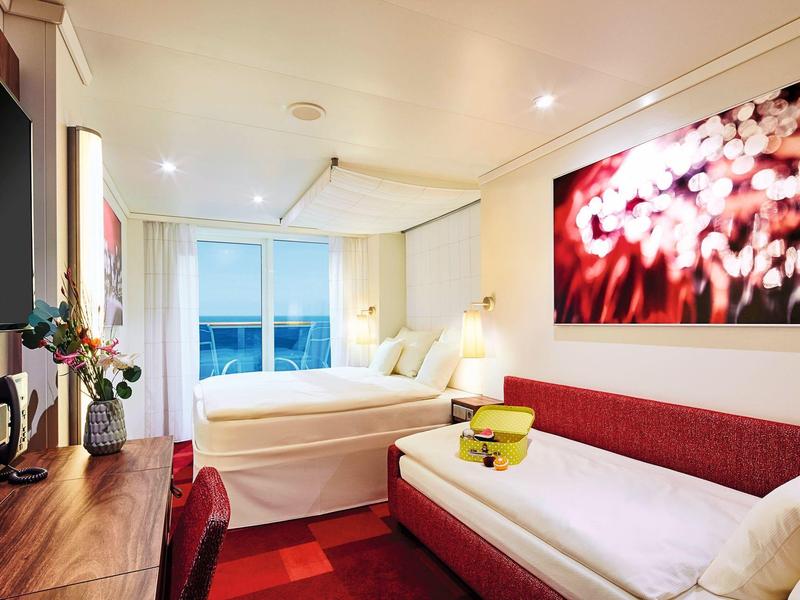 Lichte hotelkamer met twee eenpersoonsbedden, rode bank, houten bureau en grote wanddecoratie.