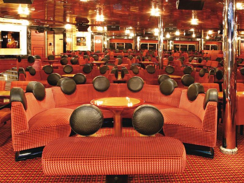 Intérieur d'un salon de croisière avec canapés rouges et coussins ronds noirs.