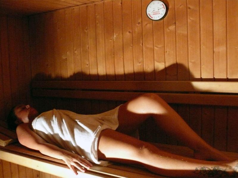 Donna che si rilassa in una sauna di legno avvolta in un asciugamano con un orologio a parete.