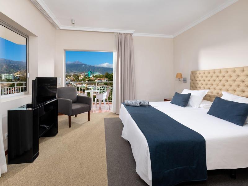 Camera d'hotel con letto matrimoniale, poltrone e balcone con vista sulle montagne