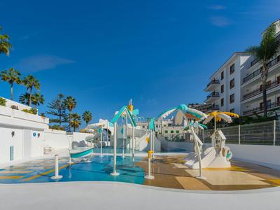 Colorful water playground with mermaid decorations beside modern hotel buildings under a blue sky.