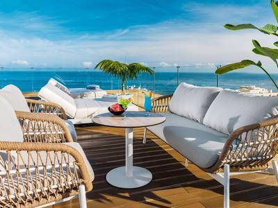 Rooftop terrace with wicker furniture and sea view under blue sky.