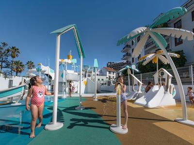 Outdoor water play area with slides, showers, and children playing under a sunny sky.