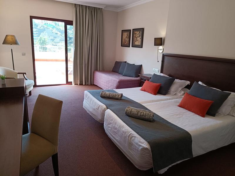 Cozy hotel room with two beds, sofa, desk, and balcony with mountain view.