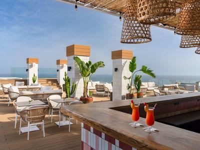 Terraza en la azotea con bar, asientos y vista al mar bajo cielo azul.