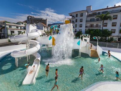 Children playing and sliding in a hotel outdoor pool with waterslides and a water splash feature.