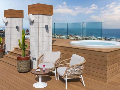 Moderne Terrasse mit Holzdeck, Whirlpool, gemütlichem Sitzbereich und Blick aufs Meer.