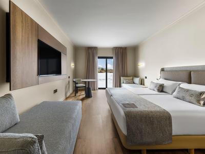 Modernes Hotelzimmer mit großem Bett, grauem Sessel und Balkon mit Blick nach draußen.