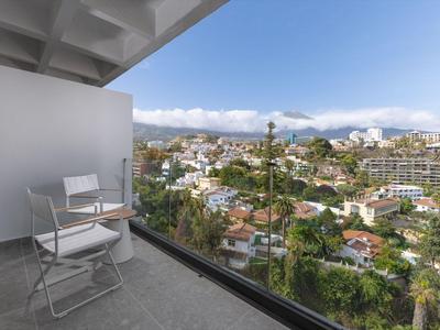 Balcone con due sedie e un tavolo, vista su una città con montagne sullo sfondo.