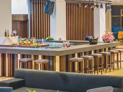 Moderne hotelbar met hoge krukken, verlichte toog en zithoek met banken en fauteuils.