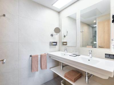 Nowoczesna łazienka hotelowa z podwójną umywalką, różowymi ręcznikami i dużym lustrem.