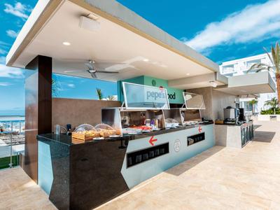 Área moderna al aire libre con buffet de hotel con comida y bebidas bajo un cielo azul.