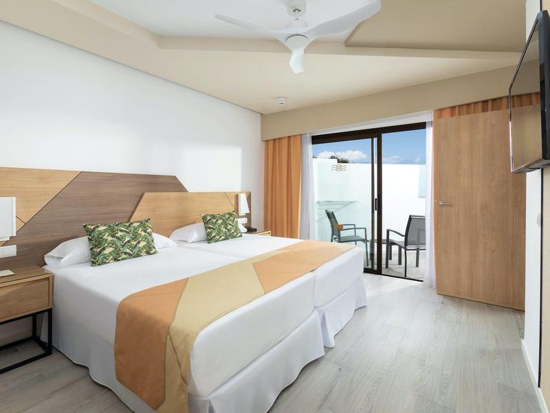 Habitación de hotel luminosa con cama doble, balcón y decoración moderna en tonos cálidos.