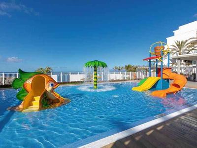 Piscine pour enfants colorée avec toboggans et fontaine sous ciel bleu.