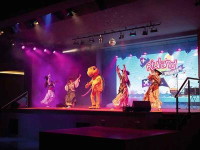 Scène avec des artistes en costumes colorés et éclairage violet lors d'un spectacle.
