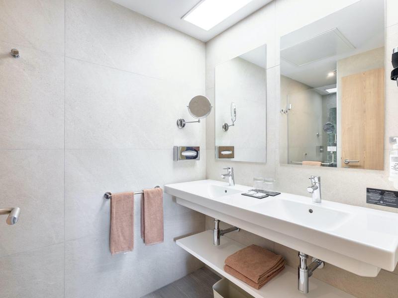 Modernes Badezimmer mit großem Spiegel, weißem Doppelwaschbecken und grauen Fliesen.