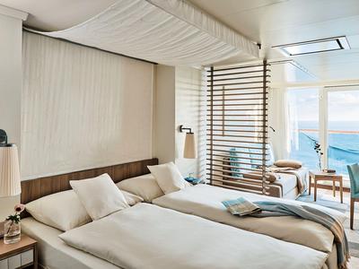 Modern hotel room with two beds, seating area, and sea view through large windows