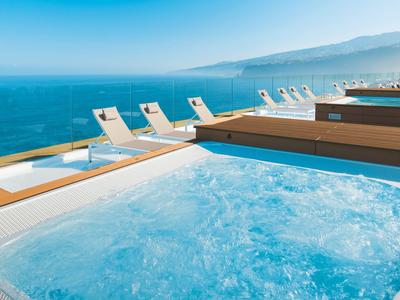 View of a bubbling hot tub with lounge chairs by the sea.