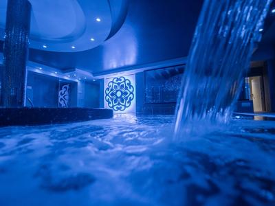 Interior view of a stylish pool with waterfall and blue lighting in a spa area.