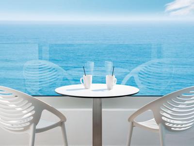 Twee witte stoelen en een tafel met twee drankjes op een balkon met uitzicht op zee.