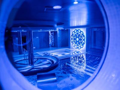 Uitzicht door een ronde opening op een moderne, blauw verlichte zwembadruimte met decoratieve patronen.