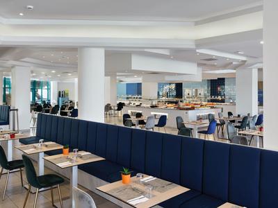 Espace de restaurant d'hôtel moderne avec bancs bleus, tables et chaises dans un cadre lumineux.