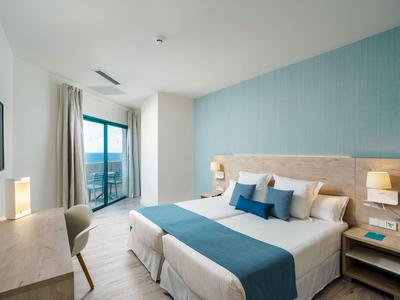 Modern hotel room with double bed, blue accents, and balcony with sea view.