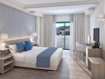Modern hotel room with double bed, desk, and balcony overlooking the sea.
