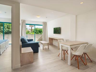 Moderne hotelkamer met woon- en slaapgedeelte, houten meubels en groot raam met uitzicht op groen.