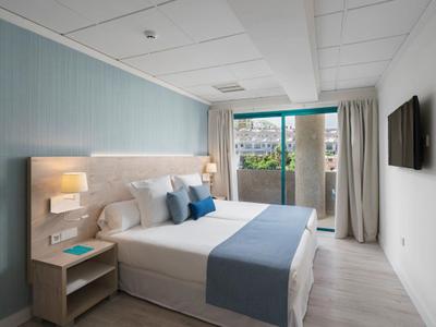 Moderne hotelkamer met tweepersoonsbed, blauwe accenten en balkon met uitzicht op groen.