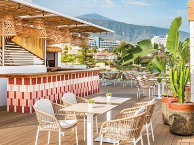 Terrace with white chairs and tables next to a bar overlooking mountains under clear sky