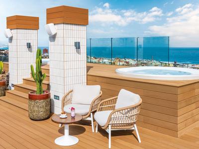 Terrace with hot tub, wood paneling, two chairs, small table, and sea view