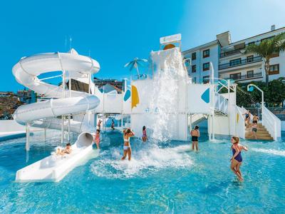 Children playing in the water park with slides and waterfalls in front of a hotel.