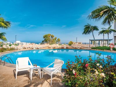 Round outdoor pool with white lounge chairs and palm trees under clear blue sky.