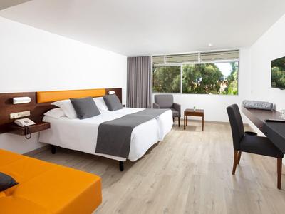 Chambre d'hôtel moderne avec lit double, canapé orange, bureau et grande fenêtre donnant sur la verdure.