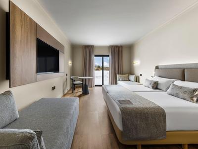 Chambre d'hôtel moderne avec lit double, coin salon, télévision et balcon avec vue mer.