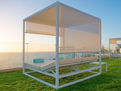 Moderne buitenlounge stoel met zonnescherm op groen gras met uitzicht op zee bij zonsondergang