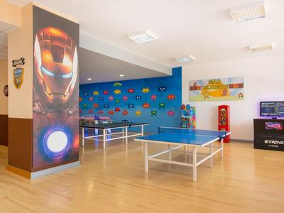 Interieur van een recreatieruimte met tafeltennistafels, kleurrijke muurdecoraties en een America Super Smash Bros arcade-spel.