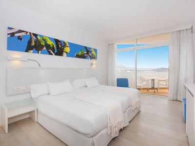 Lichte hotelkamer met tweepersoonsbed en balkon met uitzicht op de bergen.