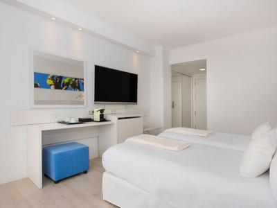 Modern hotelkamer met tweepersoonsbed, tv en blauwe poef.