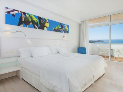 Bright hotel room with large bed, balcony, and sea view.