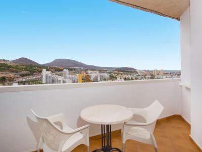 Balcony with two white chairs and round table overlooking city and mountains