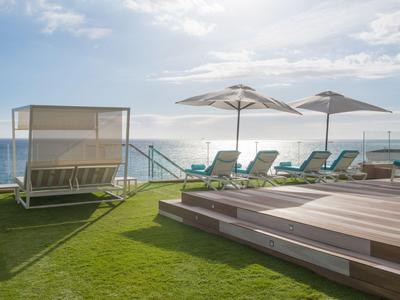 Green lawn with sun loungers, umbrellas, and sea in the background under a blue sky.