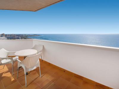 Balcony with table and chairs overlooking the sea under a clear sky.