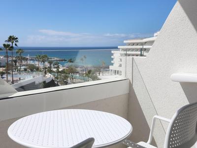 Balcony with white table and chair overlooking the sea and palm trees under a blue sky