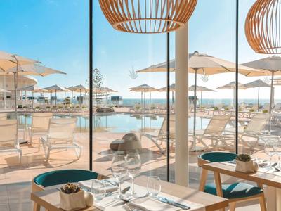 View through glass onto pool area with sun loungers and umbrellas on a sunny day.