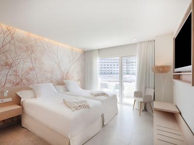 Chambre d'hôtel moderne avec deux lits, une télévision et une grande fenêtre avec rideaux.