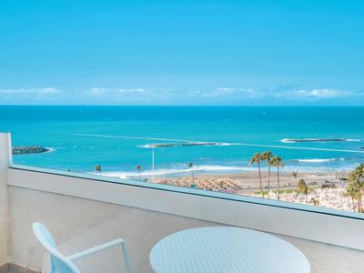 Vue d'une terrasse blanche avec table et chaise sur la mer bleue et la plage.