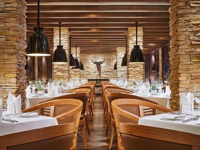 Elegantní restaurace s dřevěným stropem, kamennými zdmi a teple osvětlenými stoly.